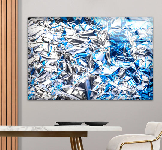 Bright highlights gleam on the crinkled silver and blue metallic texture of this glass print, perfect for abstract home decor.