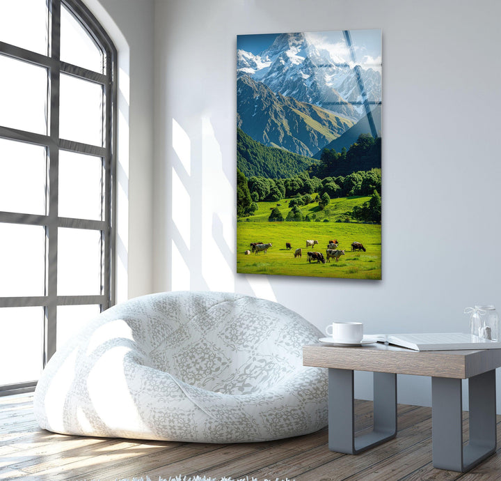 A serene countryside view with vibrant meadows and towering mountain ranges under a clear sky.
