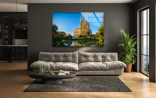 Displayed prominently, the Sagrada Familia glass wall art prints showcase Barcelona's cathedral, reflecting in the serene water beneath a clear blue sky.