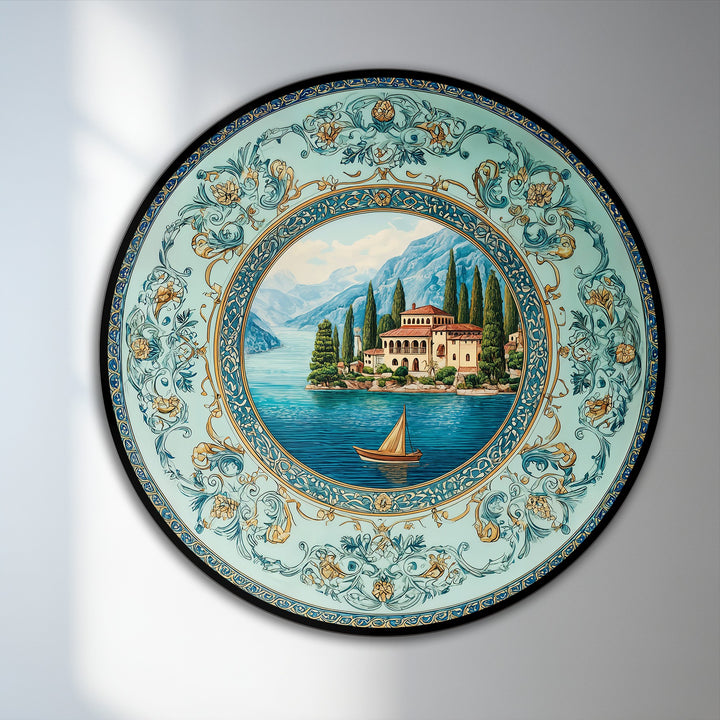 Dominating the negative space, this round oil painting artwork features an ornate, bordered view of a mediterranean villa on a turquoise lake with mountains.