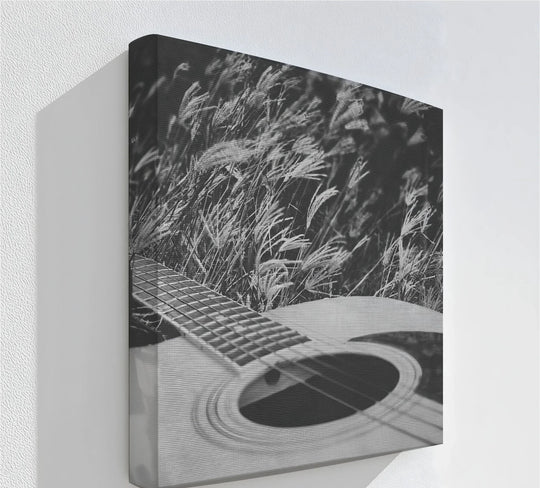 Durable material quality highlights the black and white hanging canvas print, showcasing an acoustic guitar resting peacefully within a tranquil field of tall grasses.