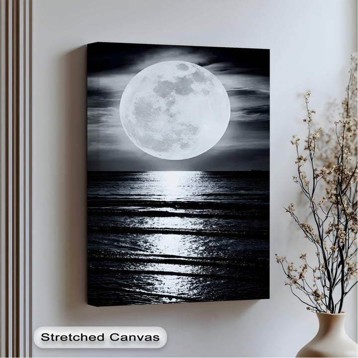 The abstract quality of this big canvas print highlights the dramatic contrast of a radiant full moon casting a shimmering path across the dark, rippling ocean.