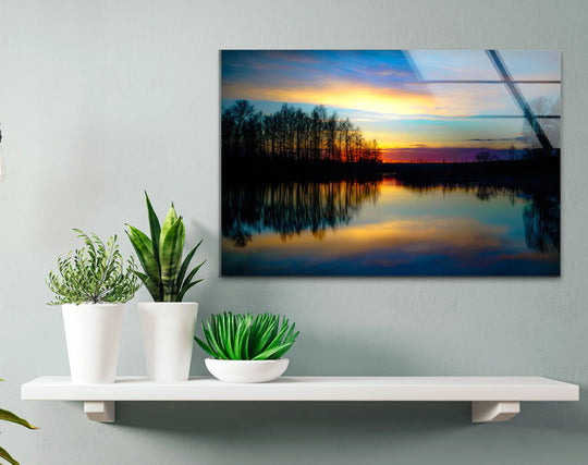 A sunset reflection glass print displays a tranquil forest and lake, featuring the sleek edges of this unique modern wall decor.