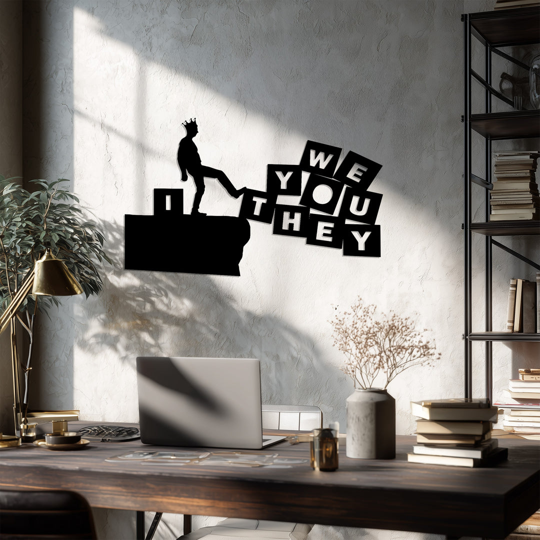 Modern black metal wall art showing man kicking “We You They” blocks