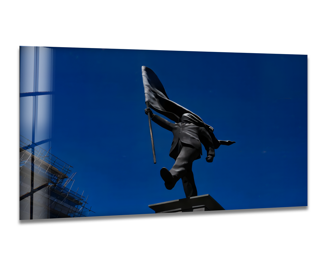 The expansive negative space of the deep azure sky enhances the dark Banksy Flag Bearer statue in this vivid tempered glass wall art.