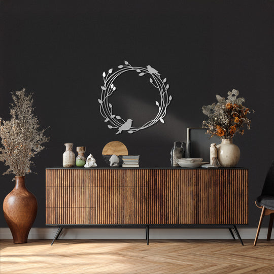 A calm mood is evoked by the Whispering Branches bird and vine metal art for wall, a round silver metal wall art casting soft shadows in a serene interior setting.