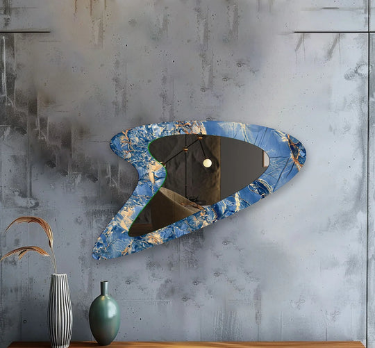 Asymmetric mirror in an abstract blue and gold marble pattern with an irregular shape reflecting an entryway on a grey concrete wall
