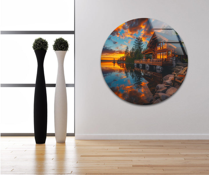 Glass wall art featuring a cozy lakeside cabin illuminated by a stunning sunset.
