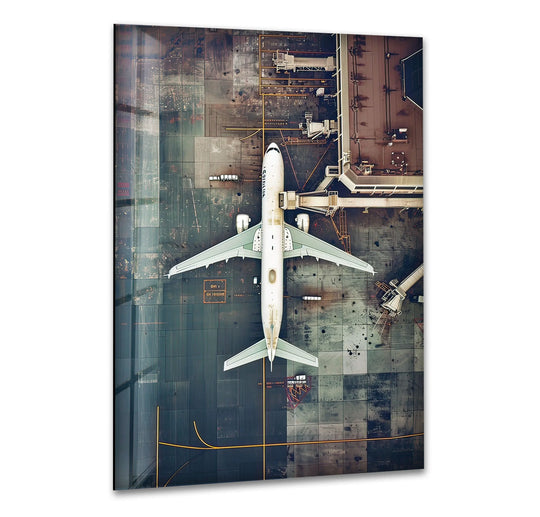 An aerial view of a long airplane forms a striking glass art painting, showcasing the organic shapes of the tarmac and jet bridge.