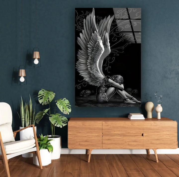 High-contrast black and white glass art showing an angel with large wings curled up on a stone floor.