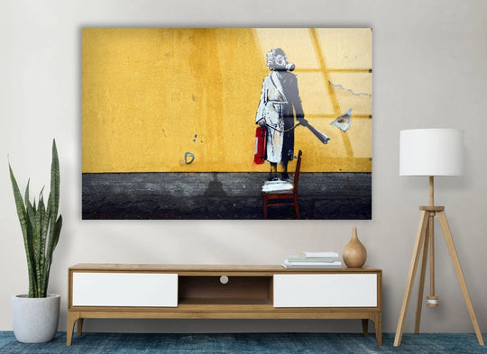 Banksy Woman with Gas Mask glass wall art with a red fire extinguisher against a yellow wall a modern piece of urban Banksy wall art