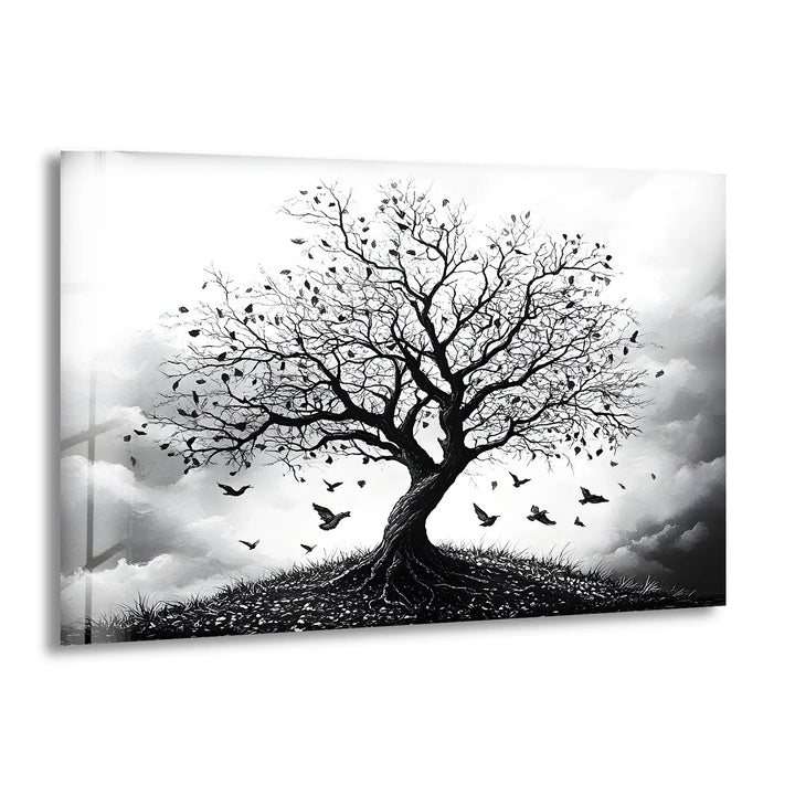 Black and white glass wall art featuring a solitary tree with falling leaves and birds flying against a cloudy sky.