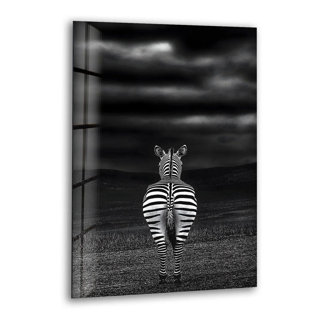Black and white glass wall art featuring a zebra standing alone, viewed from behind under a dramatic cloudy sky.