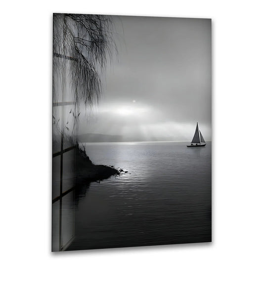 Black and white glass wall art of a sailboat drifting on calm water under soft sun rays.