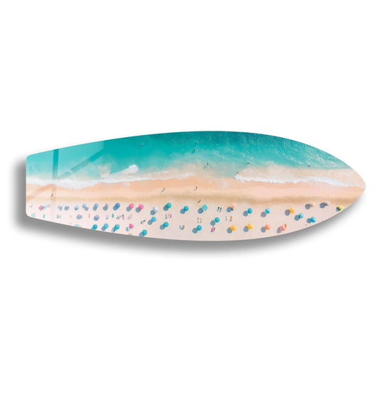 Smooth surface texture defines this tempered glass wall art of a surfboard featuring an aerial beach scene with umbrellas and the glistening ocean.