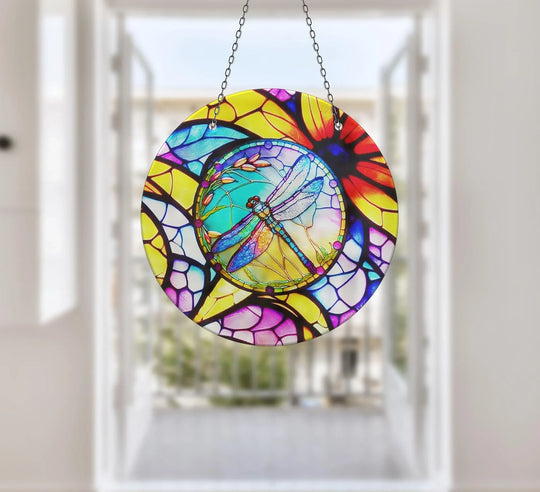 Foregrounding a stained glass suncatcher featuring a dragonfly, the design offers intricate depth and layers accentuated in this vibrant hanging wall art.