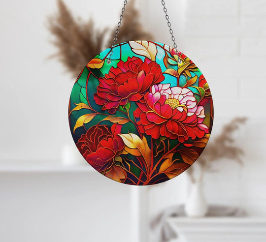 Blurred out in the background, a subtle display shelf and decorative plant complement the hanging glass wall art decor of a red flower suncatcher.