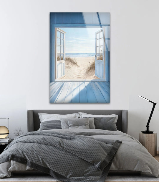 Glass wall art captures a layered beach scene through open doors with sand dunes and distant surf.