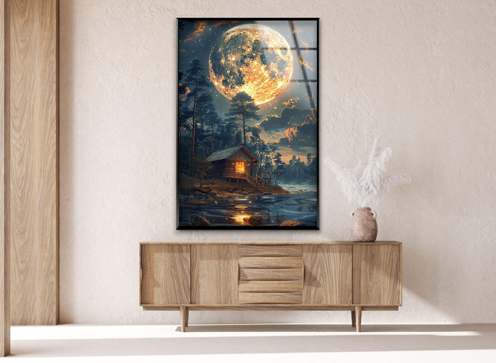 Glass wall art displaying a warm-lit cabin under a starry night sky.
