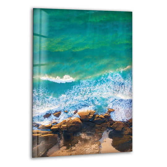 Glass wall art featuring a visual rhythm of aqua currents and crashing surf over rugged coastal rocks.