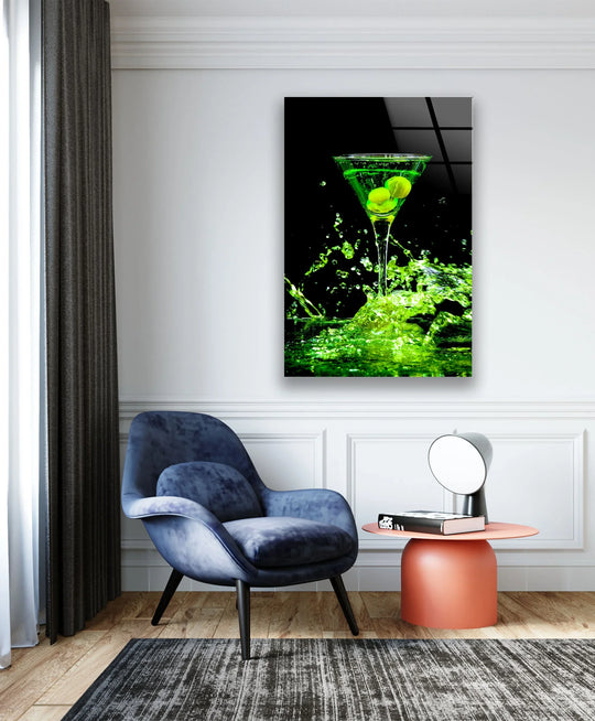 Vibrant green martini with olives glass wall art displayed vertically above a blue armchair in a modern living room setting.