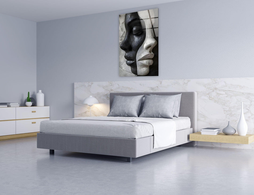 Monochrome glass artwork portraying two sculpted female faces merged into a single abstract composition.
