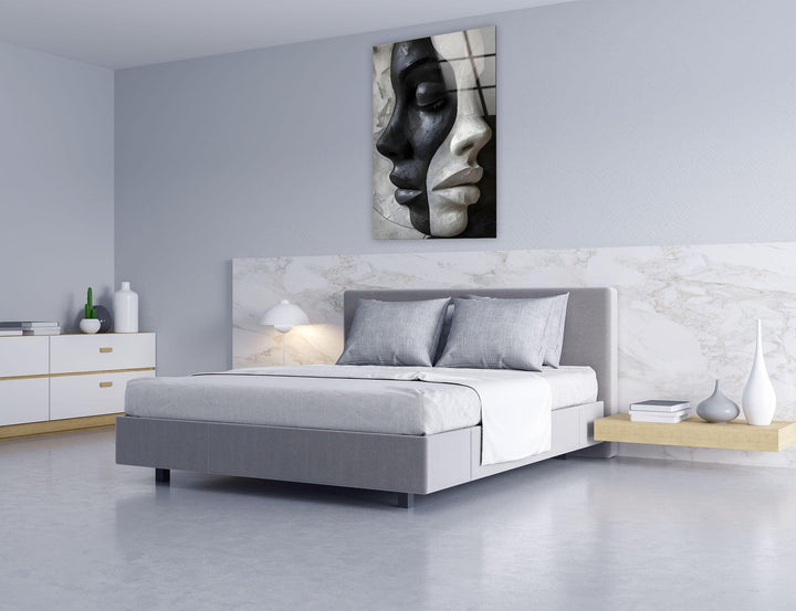 Monochrome glass artwork portraying two sculpted female faces merged into a single abstract composition.