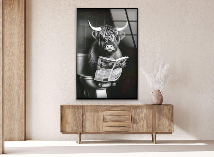 Playful grayscale wall art of a highland cow sitting on a toilet with a newspaper in hand.