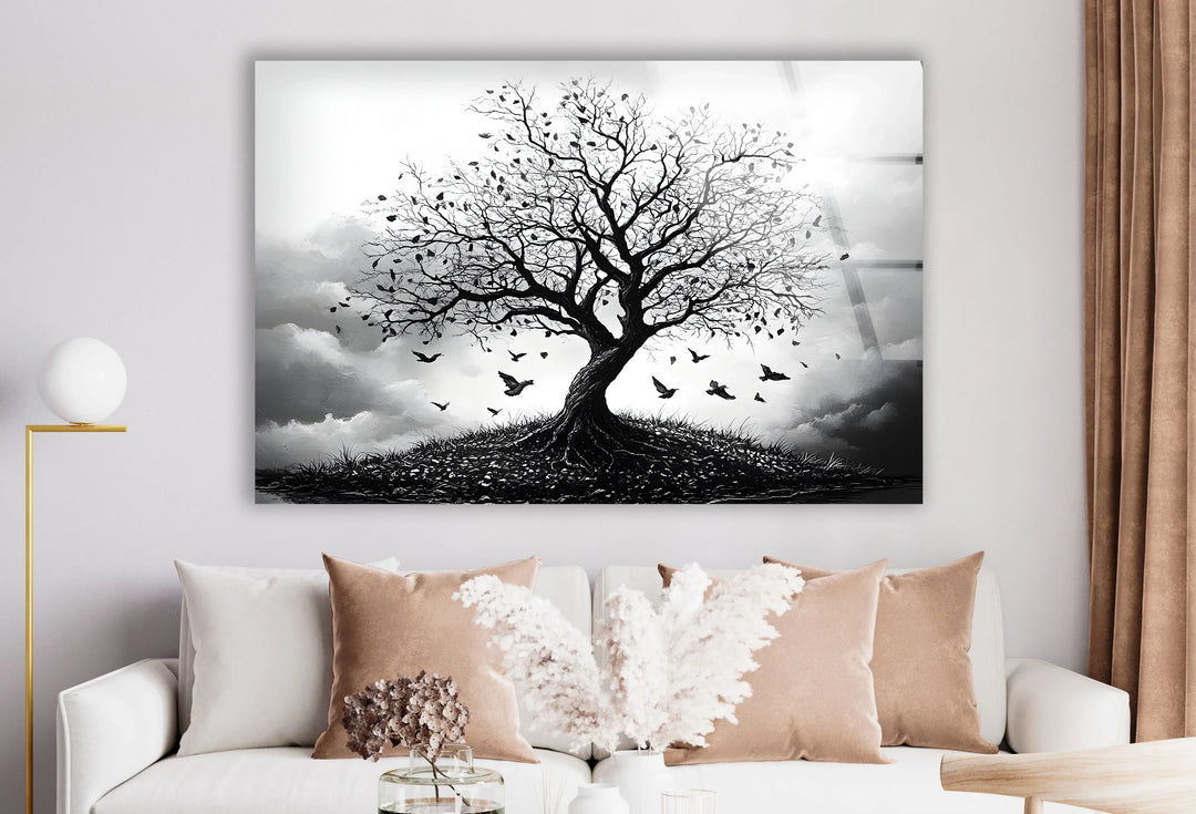 Dramatic black and white landscape on glass showing a bare tree on a hill surrounded by flying birds.