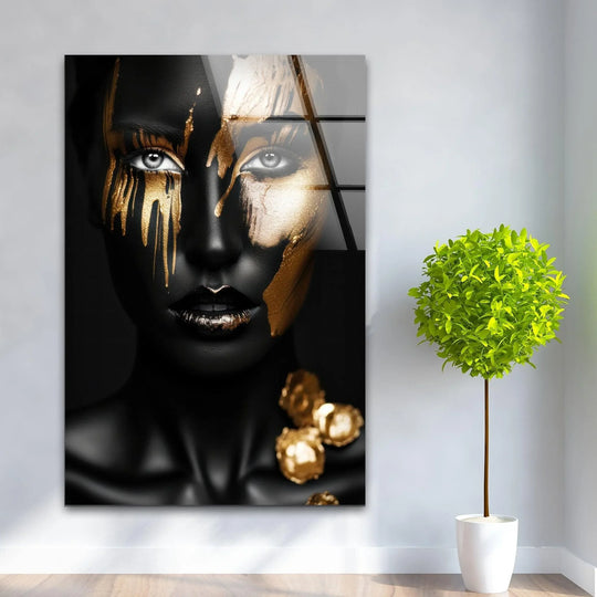 A bold black and gold woman's face, rendered in cool-toned glass wall art home decor, drips with metallic intensity.