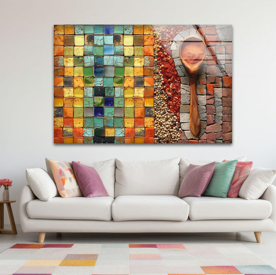 Horizontal glass wall art featuring a mosaic pattern and wooden spoon with herbs displayed above a cream sofa in a living room.