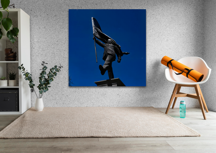 Experience the high-gloss finish of this glass wall art, a unique modern wall decor piece featuring the Banksy Flag Bearer against a vibrant deep blue sky.