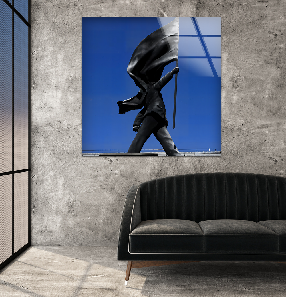 A dark, plush, channel-tufted sofa with slender wooden legs is prominent in the foreground, below the impactful Banksy art from glass.