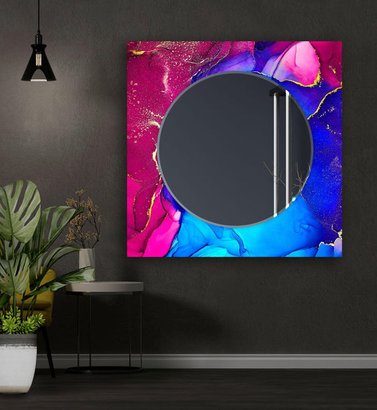 A round abstract wall mirror featuring a vibrant blue and pink design with gold accents and a smooth tempered glass surface