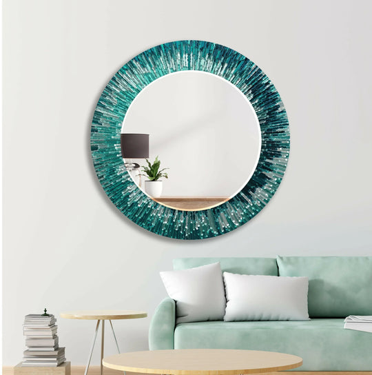 Round mirror with a turquoise abstract frame design offering modern statement decor on a white wall above a green sofa