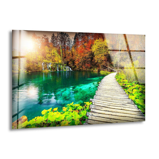 Depicting the organic forms of a serene emerald lake surrounded by autumn trees and a wooden path, this nature glass wall art captures the best glass art.