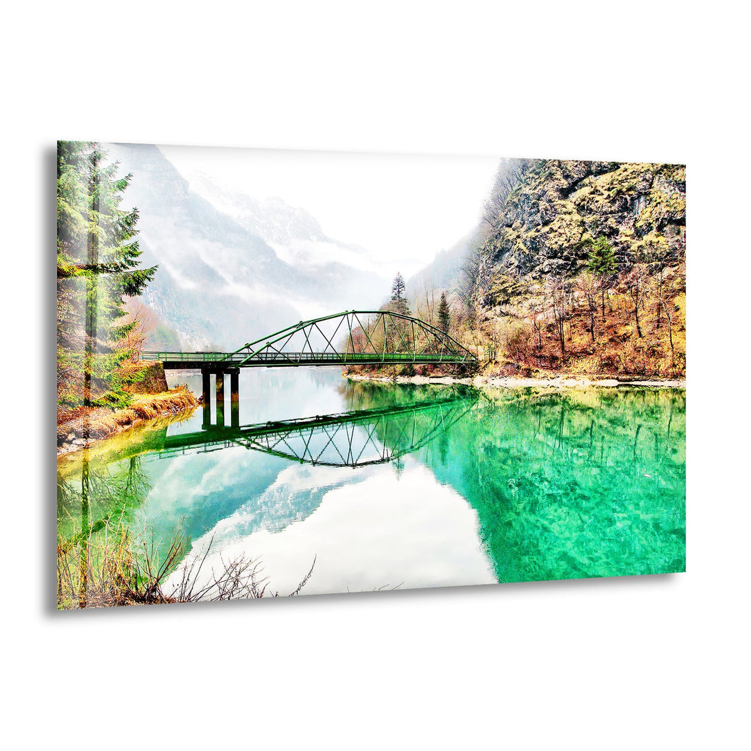Emerald River Bridge Glass Wall Art featuring a tranquil green river and a scenic mountain backdrop.
