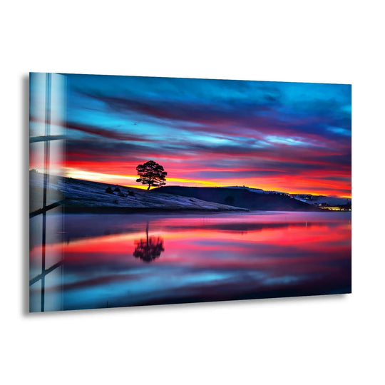 The darkest area highlights the reflective surface of this glass wall art featuring a solitary tree at sunset, perfect as stylish wall prints.