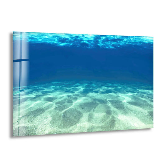 Geometric patterns of light refract through the tranquil blue water onto the sandy ocean floor in this serene underwater glass wall artwork.
