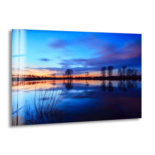 Negative space defines the reflective lake surface in this serene blue sunset landscape, a modern glass wall art decor print adding calm to interiors.