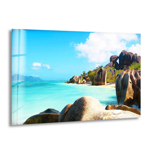 In the background, puffy white clouds drift across an azure sky above turquoise waters and a tropical granite beach, complementing the home decor of this coastal glass print.