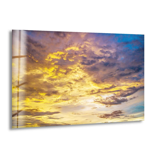 Dramatic color contrast defines this glass decorative wall art, showcasing a golden cloudscape with radiant yellow highlights against a deep blue and violet sunset sky.