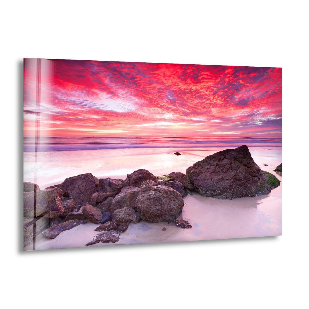 Vibrant pink sunset over a rocky shoreline captured on glass wall art.
