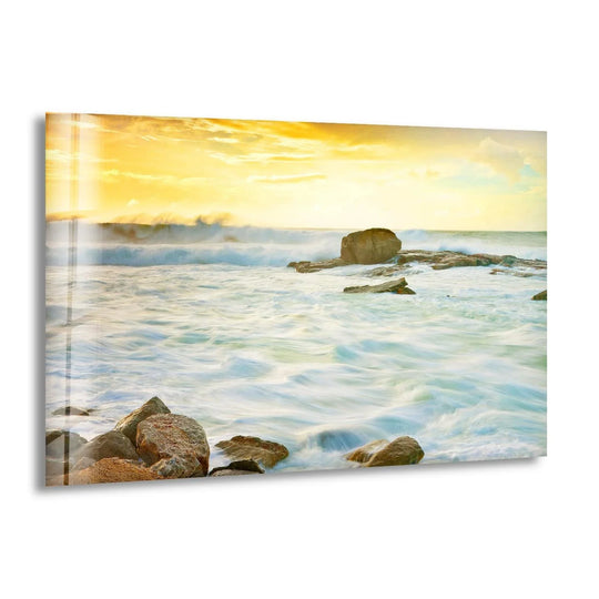 This horizontal glass wall art shows golden waves and ocean rocks under a sunrise sky and it is coastal glass wall art with a serene ocean scene and golden light