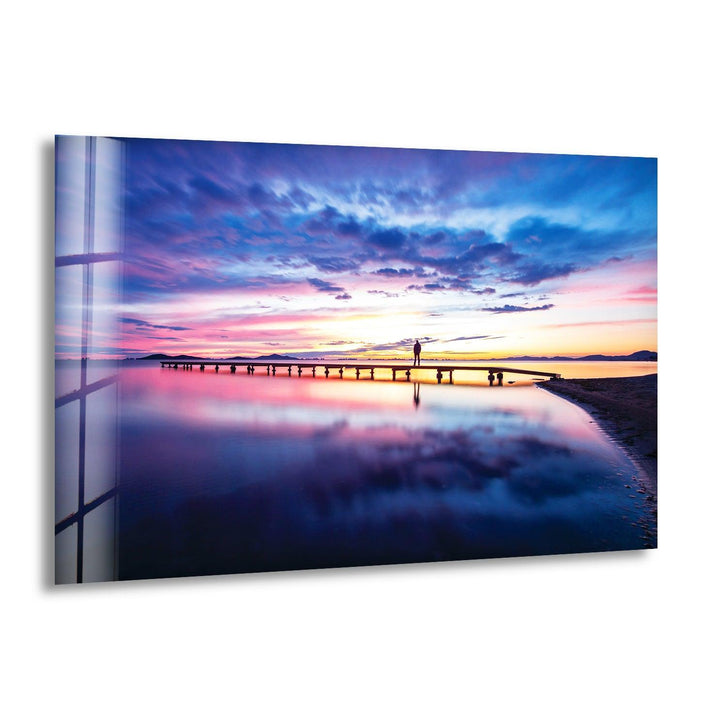 Glass wall art featuring a stunning sunset pier reflecting over calm ocean waters.
