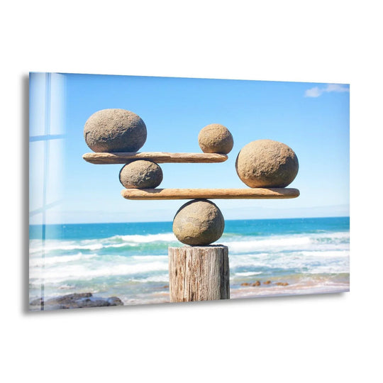 A vibrant glass wall art piece showcases saturated blues of the ocean and sky above perfectly balanced stones.