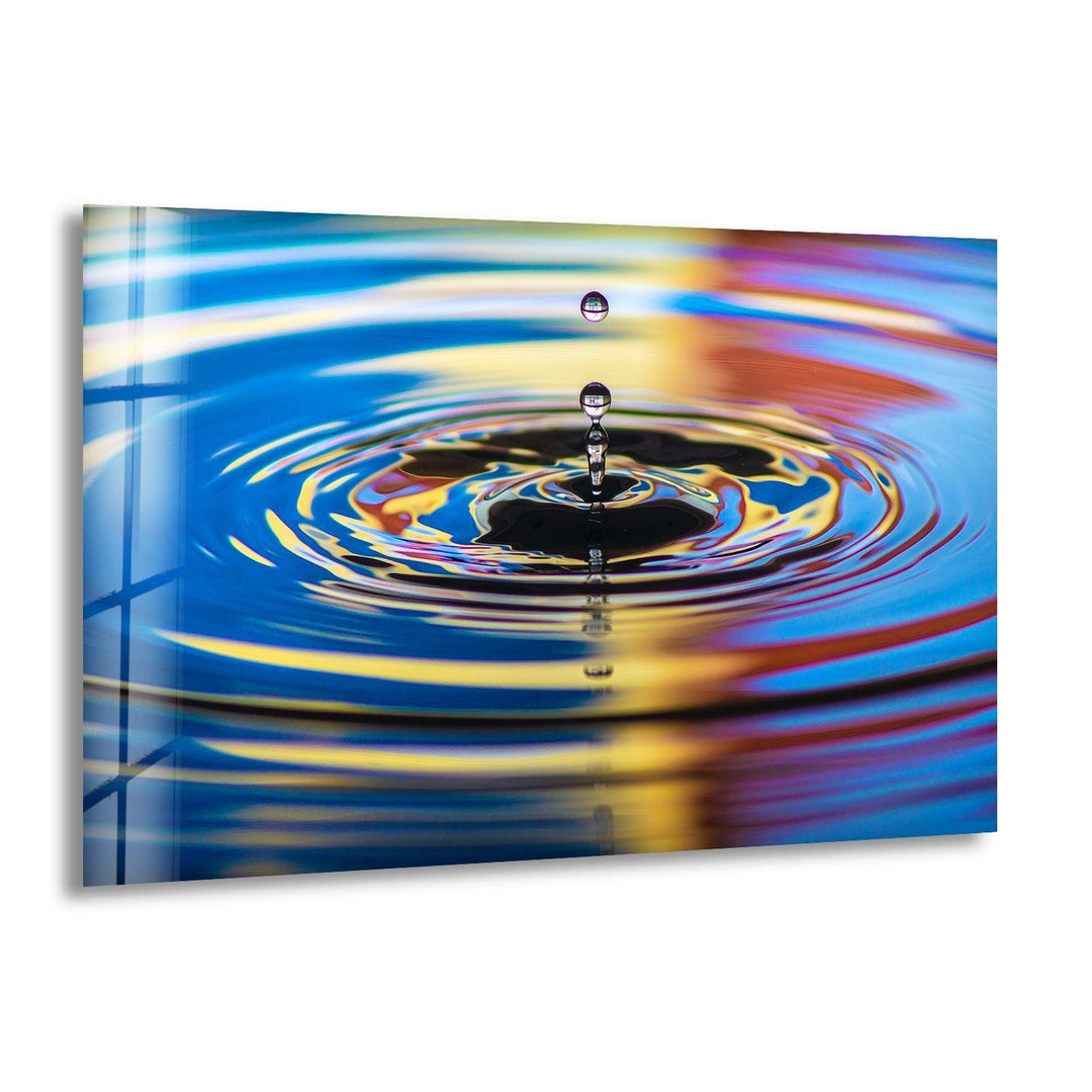 Abstract glass wall art featuring a rippling water droplet in vibrant blue and gold tones.
