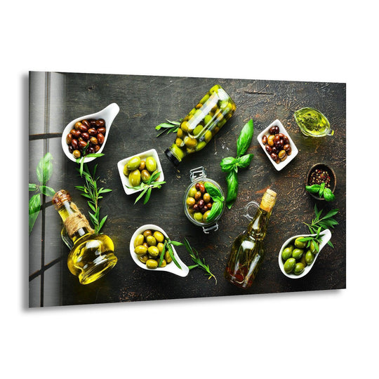 Horizontal glass wall art depicting a still life of olives, oil bottles, and fresh herbs on a dark rustic surface for modern kitchen decor.