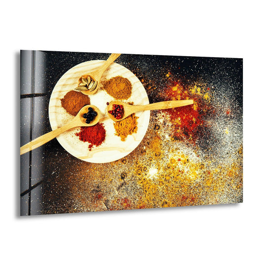 Horizontal glass wall art featuring vibrant yellow and red spices arranged on a white plate with bamboo spoons against a dark speckled background.