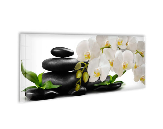 Zen Stones and White Orchid glass wall art displays stacked black stones and delicate white blooms and offers modern wall decor for a tranquil spa aesthetic